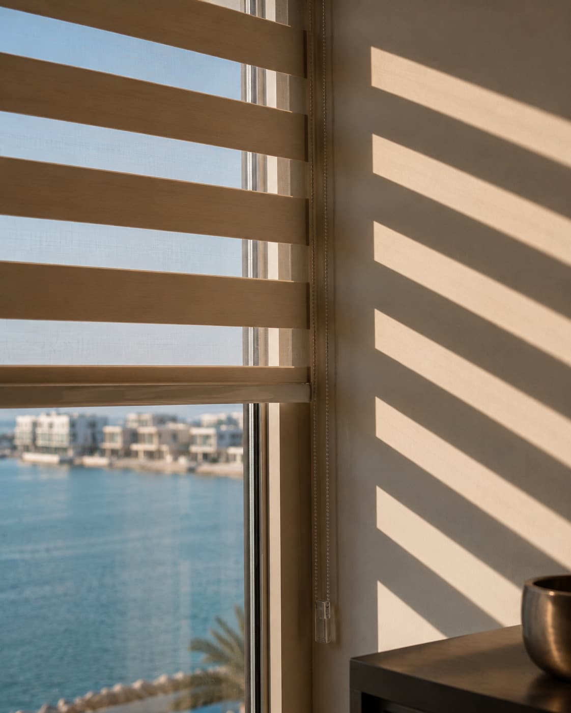 Blind half-drawn over a waterfront window, striped light on the wall